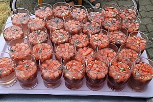 Mehrere Gläser mit einem Getränk, das mit kleinen Fruchtstücken und Kräutern gefüllt ist, auf einem Tablett angeordnet