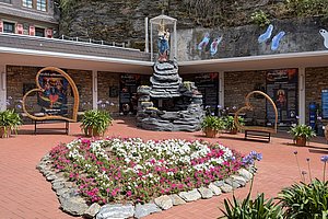 Innenhof mit Blumenbeet in Herzform, umgeben von Felsen und einer Statue in einer Glasvitrine auf einem Felsenstapel