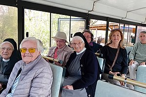Mehrere Personen sitzen in einem Bus mit großen Fenstern und grüner Polsterung
