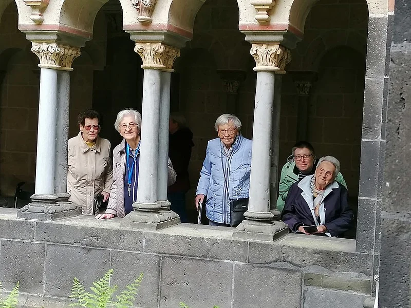 Gruppe älterer Menschen steht hinter einer steinernen Balustrade mit Säulen in einem historischen Gebäude