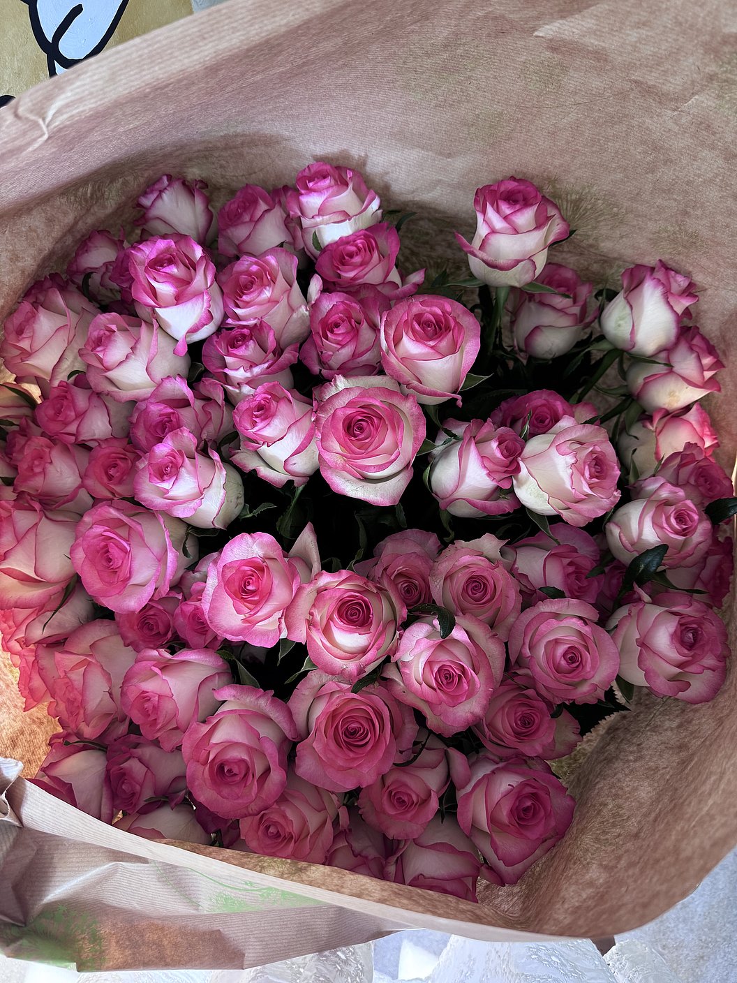 Ein großer Strauß rosa-weißer Rosen in braunem Papier eingewickelt