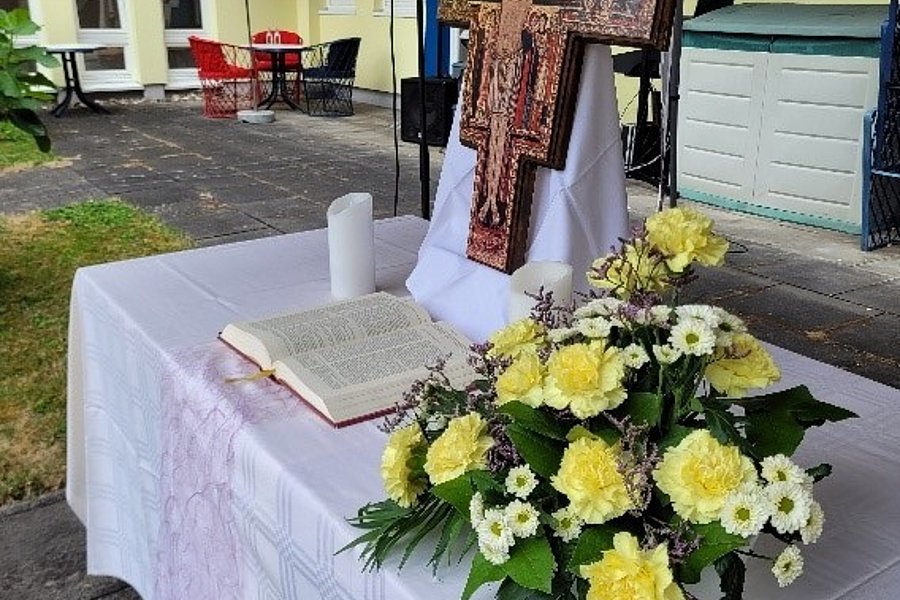 Altar mit weißem Tuch, offenem Buch, Kerze, Blumenarrangement und hölzernem Kruzifix im Innenhof eines Gebäudes